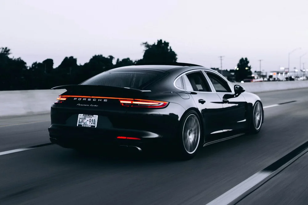 A dark sedan equipped with dark car tint traveling smoothly down a multi-lane highway at dusk, captured with motion blur on the wheels and protected by an invisible clear bra.