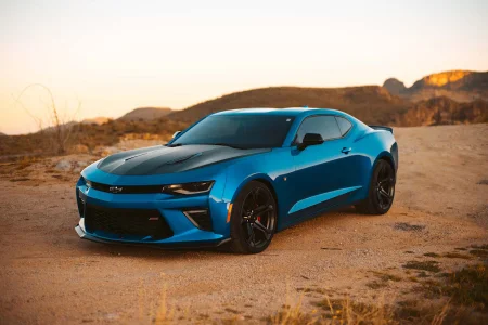 A vivid blue sports coupe with premium window tinting parked on a gravel hill during sunset, emphasizing rugged outdoor lighting and paint protection film body lines.