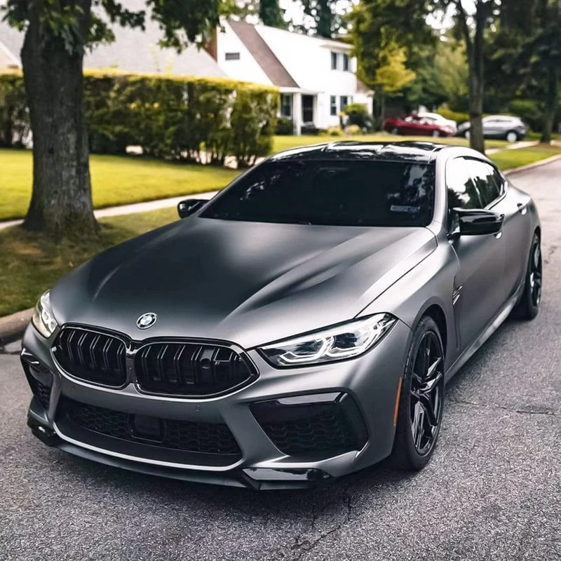 A sleek luxury sports sedan parked on a residential street, showcasing a full satin black vinyl wrap and professional auto window tinting.